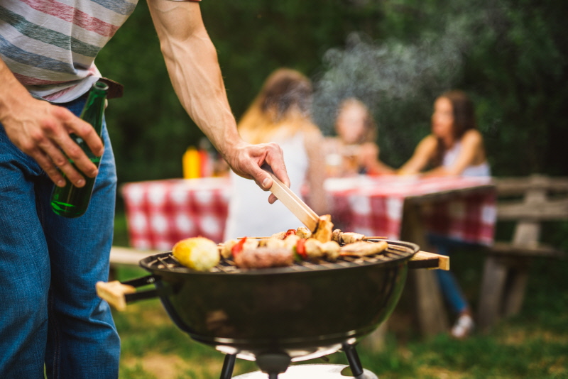 Close up of a man making barbecue and holding beer bottle.